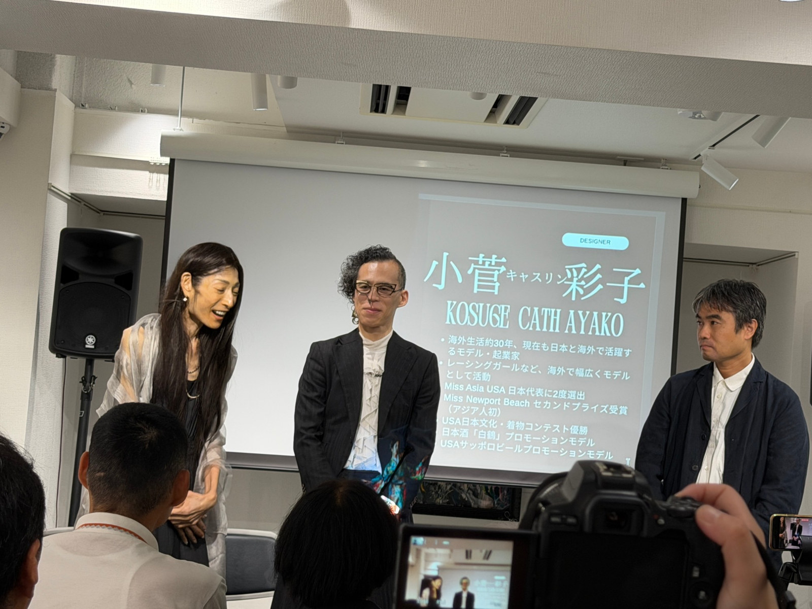 登壇された小菅キャスリン綾子さん、平林景さん、矢野雷太先生。スクリーンには小菅さんのプロフィールが映されていました