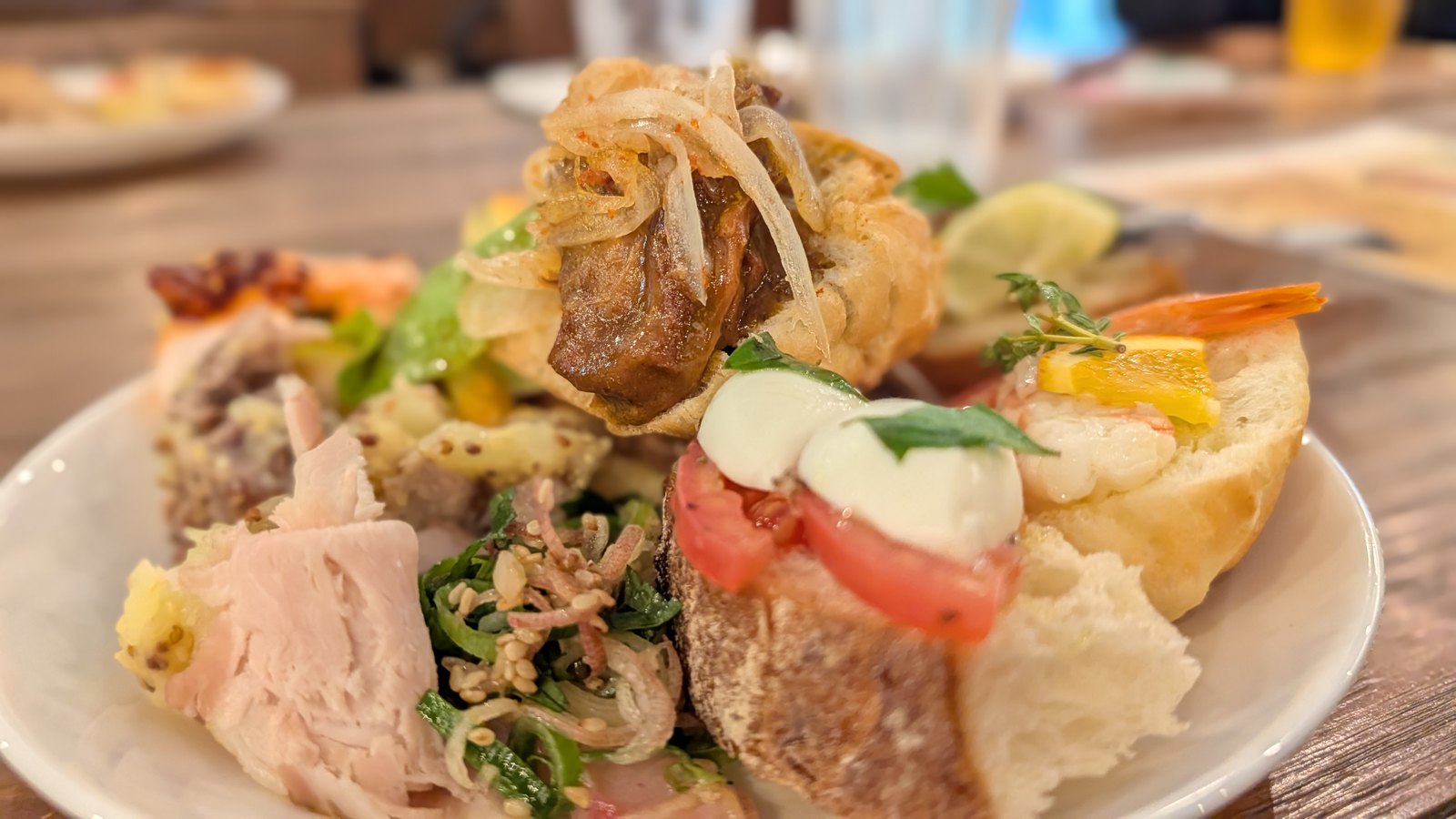 ローストした豚肉、トマトとモッツァレラ、エビをのせたパン、煮込んだ肉をのせたパンなどを盛った皿